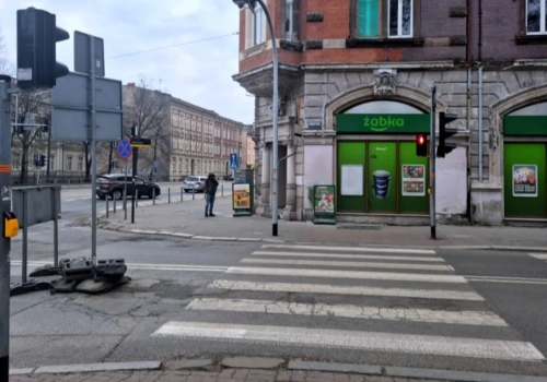 Droga zamknięta, ale piesi stoją i czekają na zielone. Samochodów prawie nie ma